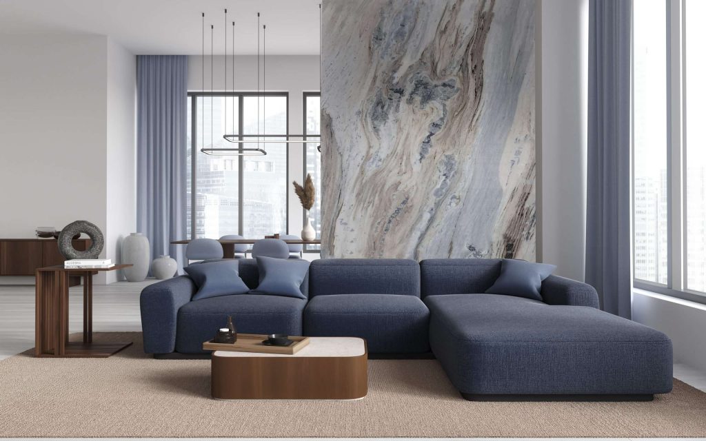Modern living room with a large blue sectional sofa and a floor-to-ceiling Portinari marble accent wall featuring soft beige and gray flowing patterns.