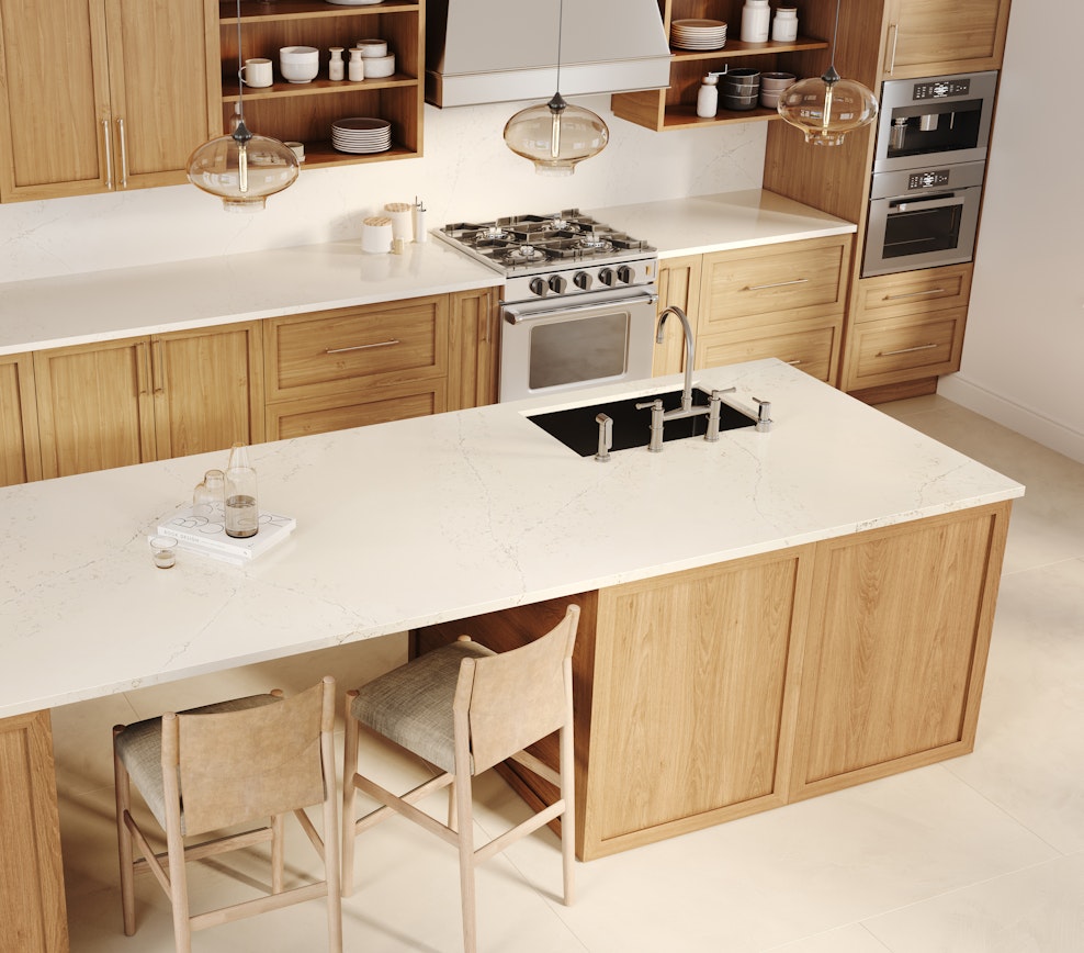 Bright kitchen with Siberian Frost quartz countertops, light wood cabinets, kitchen island, stove, oven, and bar stools.