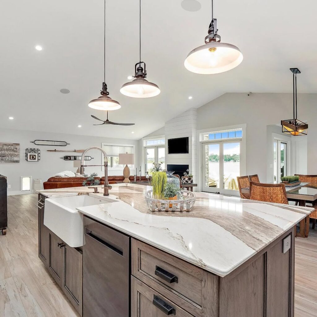 Spacious open-concept kitchen with large island, farmhouse sink, pendant lights, and living area in the background.