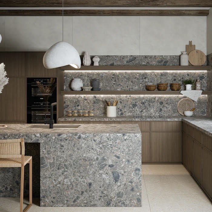 Modern kitchen with gray Dekton countertop and backsplash, dark wood cabinets, black oven, white pendant light, and bar stool.